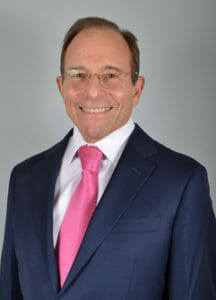 James Stuzin, M.D. Smiling in a black blazer, white shirt, and pink tie.